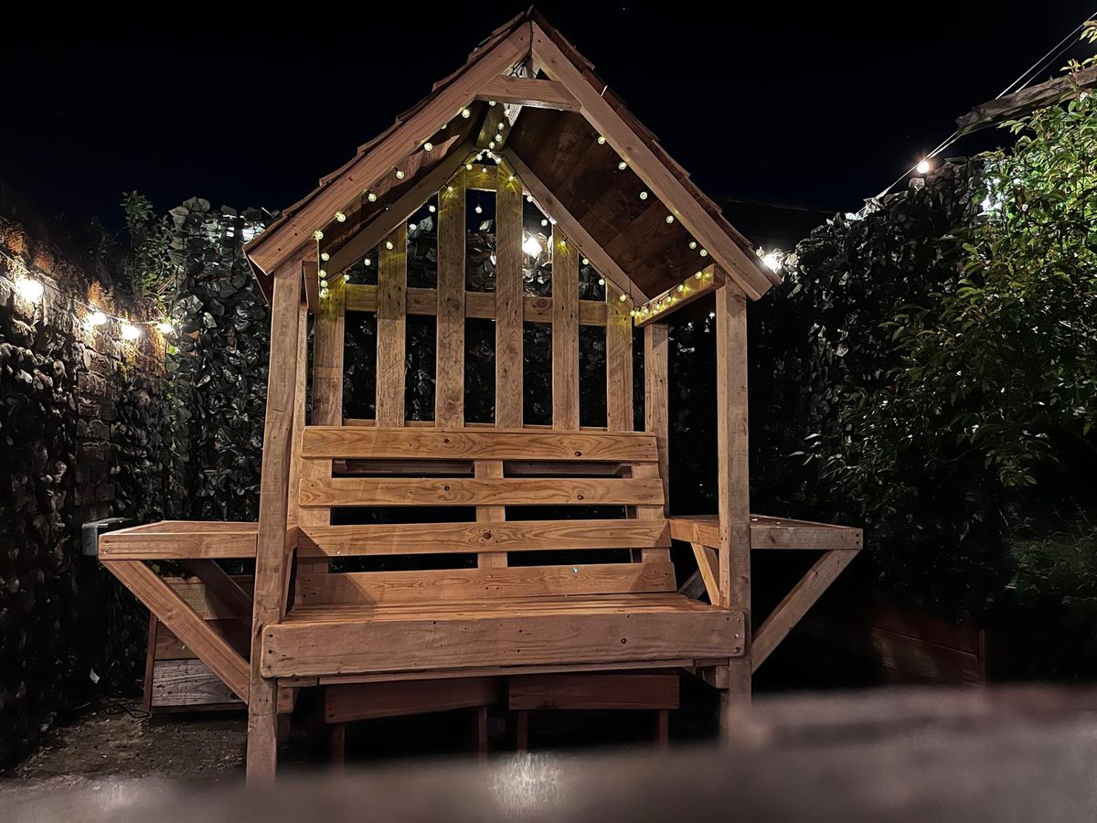 Wooden bench shelter wrapped in fairy lights and ivy